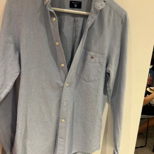 Ljusblå oxfordskjorta från GANT - Klassisk ljusblå oxfordskjorta från GANT med button-down krage och bröstficka med broderad logga. Skjortan har lång ärm och stängs med vita knappar framtill. Regular fit för en bekväm passform.