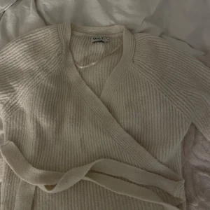Beige omlottkofta från ONLY - Mysig beige stickad omlottkofta från ONLY med knytskärp i midjan. Tröjan har lång ärm och ribbad struktur