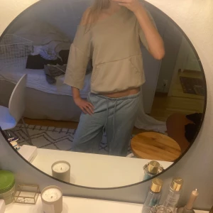 Beige offshoulder sweatshirt - Säljer en beige sweatshirt med offshoulder-design och trekvartsärmar. Tröjan har en avslappnad passform och en stor ficka framtill. Perfekt för en chill och trendig look.