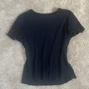 Svart ribbad topp från Ellen New York - En svart ribbad topp från Ellen New York med rund halsringning och korta ärmar. Enkel och stilren design som passar till mycket. Materialet är stretchigt och följsamt. 160=S❤️