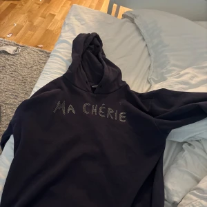 Marinblå hoodie från Gina Tricot - Säljer en marinblå  hoodie från Gina Tricot med texten 'MA CHÉRIE' i små glittriga stenar framtill. Tröjan har huva och en klassisk, avslappnad passform. Perfekt för en chill och trendig look. Inga defekter, andvänd ett fåtal gånger, i storlek 158/164 men skulle säga att den är som en strl S