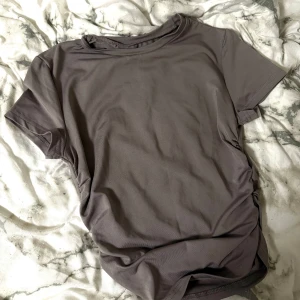 Grå t-shirt med rynkade detaljer - Säljer en grå t-shirt med korta ärmar och snygga rynkade detaljer på sidan. Perfekt för en chill och stilren look. T-shirten har rund halsringning och är gjord i ett mjukt material.