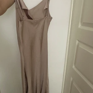 Champagnefärgad långklänning med smala axelband,oanvända klänningar  - Säljer en elegant långklänning i champagnefärg med smala axelband och draperad halsringning. Klänningen har en mjuk, följsam passform och är perfekt för sommarens tillfällen.