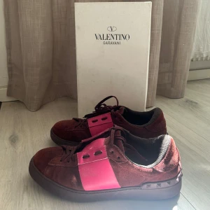 Valentino Open - Säljer ett par snygga Valentino sneakers i vinröd mocka med breda rosa paneler och svarta detaljer. Skorna har snörning och en unik design med mönstrad sula baktill. Perfekta för dig som vill sticka ut med din stil. Box ingår