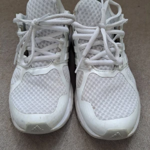 Vita Adidas sneakers med mesh och cloudfoam - Säljer ett par vita Adidas sneakers med mesh-ovandel och cloudfoam-sula. Skorna har snörning och klassiska tre ränder på sidan. Perfekta för dig som gillar sportig stil och vill ha bekväma skor till vardagen. Jätte mjuka och sköna, saknas dock innersula då jag haft egen anpassad sula, hittar tyvärr inte originalet men funkar med vilken sula du vill. 