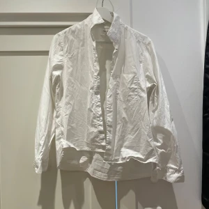 Vit skjorta från Filippa K - Klassisk vit skjorta från Filippa K med enkel bröstficka och knappar framtill. Skjortan har lång ärm och är tillverkad i ett mjukt bomullsmaterial. Perfekt för en stilren och clean look.