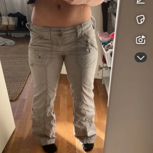 Gråa byxor från EDC - Säljer ett par gråa cargopants med flera fickor och snygga knappar både fram och bak. Byxorna har låg midja och är bootcut med detaljerade sömmar. Perfekta för en avslappnad och trendig stil. Dom är även sudda lågmidjade men inget som märks och går att sprätta upp! 