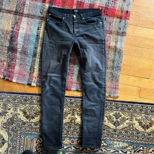 Svarta jeansbyxor från A.P.C. Petit Standard - Säljer ett par svarta jeansbyxor från A.P.C. Petit Standard. Modellen har smal passform, klassisk femficksdesign och silverfärgade knappar. Perfekta för dig som gillar stilrena och tidlösa jeans. I storlek 30