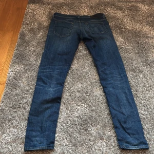 Mörkblå jeans från tiger of sweden - Säljer ett par klassiska mörkblå jeans med raka ben och fem fickor. Byxorna har normal passform och stängs med dragkedja och knapp. Perfekta till vardags och passar till det mesta. Snygg slitning på framsidan för en trendig look. 32/32