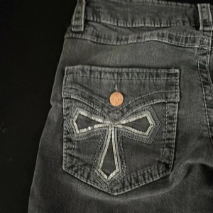 Svarta jeansbyxor från Gina Tricot med broderade bakfickor - Svarta jeansbyxor från Gina Tricot med snygga broderade detaljer på bakfickorna och kopparfärgade knappar. Klassisk femficksmodell och dragkedja framtill. Perfekta för dig som gillar en cool och stilren look.