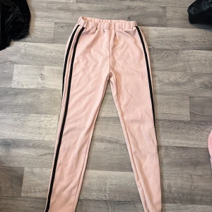 Rosa hoodie med rosa byxor från SHEIN - Säljer en ljusrosa hoodie från SHEIN med svart tryck '86 FREEDOM' på bröstet och svarta ränder på ärmarna. Hoodien har trekvartsärm och är tillverkad i ett mjukt syntetmaterial. Perfekt för en avslappnad stil. Och byxorna har svarta ränder på sidan