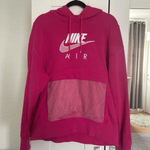 Rosa hoodie från Nike Air - Säljer en snygg rosa hoodie från Nike Air med vit logga och stor meshficka framtill. Tröjan har huva med dragsko och långa ärmar. Perfekt för en sportig och avslappnad stil.