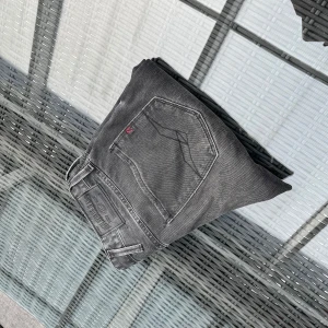 Svarta jeansbyxor från Replay - Säljer ett par svarta Replay jeans med klassisk femficksdesign och snygga detaljer på bakfickorna. Jeansen har en diskret logotyp på bakfickan och är perfekta för dig som gillar en stilren look.