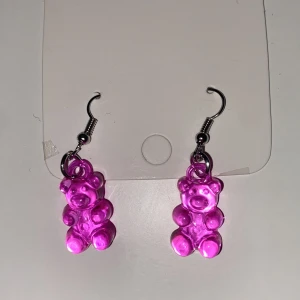 Rosa björngodis örhängen INGA PLUPPAR - Säljer ett par söta örhängen med rosa björngodis-berlocker. Hängena är i plast och krokarna i metall. Perfekta för dig som vill ha något lekfullt och färgglatt till din stil.