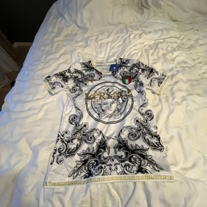 Vit och svart t-shirt från Puma x Italien - Säljer en riktigt snygg t-shirt från Puma med officiellt Italien-märke. T-shirten är vit med svart barockinspirerat mönster och gulddetaljer, samt broderad Italiensk landslagssköld på bröstet. Perfekt för dig som gillar unik stil och fotboll. S i tröjan men lite mer som M, pris är förhandlingsbart. Ny!