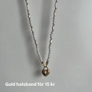 Halsband med hjärthänge och pärlor - Snyggt halsband med vita pärlor och små guldfärgade detaljer. Hänget är ett litet guldfärgat hjärta med en rosa detalj i mitten. Perfekt accessoar för att lyfta din outfit.
