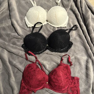 3-pack spetsiga bh-toppar i vitt, svart och vinrött - Säljer tre bh-toppar med spetsdetaljer i färgerna vit, svart och vinröd. Alla har vadderade push up kupor och justerbara axelband. Den svarta har små pärldetaljer längs kanten, som lossnar lätt, och den vinröda har en liten pärla framtill samt band som går över kupan på brösten. OBS den vita är i 70C, de andra 75C. OBS ENDAST DEN SVARTA KVAR❤️