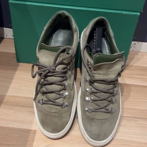 Olivgröna mockasneakers från Diemme - Säljer ett par olivgröna sneakers från Diemme i mocka med gröna detaljer och robust snörning med metallöglor. Skorna har vit platt sula och rund tå, perfekt för dig som gillar stilrena men ändå unika sneakers.