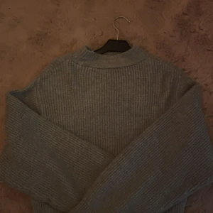 Grå stickad tröja från Gina Tricot - Mysig grå stickad tröja från Gina Tricot i storlek S. Tröjan har ribbad struktur, hög hals och långa ärmar. Perfekt för lager-på-lager och chill dagar. Enkel att matcha med jeans eller kjol.