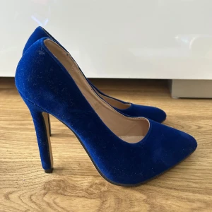 Blå sammetspumps med klack - Säljer ett par eleganta pumps i djupblå sammet med hög klack och spetsig tå. Perfekta för att lyfta vilken outfit som helst med sin lyxiga känsla och trendiga färg. Skorna har en klassisk siluett och är riktigt snygga på foten. De är helt oanvända storlek 35 men skulle säga snarare 36