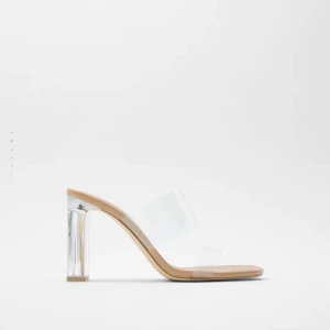 Beiga klackskor med transparent rem - Säljer ett par snygga klackskor i beige med transparenta remmar och klack i akryl-look. Skorna har öppen tå och fyrkantig form framtill, vilket ger en modern vibe. Perfekta för dig som gillar stilrena och trendiga skor.