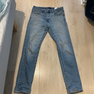Blå jeans från Uniqlo - Klassiska blå jeans från Uniqlo med normal passform och raka ben. Jeansen har fem fickor, dragkedja och knapp i midjan. Tillverkade i bomull med lite elastan för extra komfort. Perfekta för en avslappnad stil.