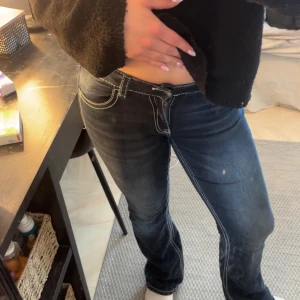 Mörkblå jeansbyxor från Gina Tricot - Säljer ett par mörkblå jeansbyxor från Gina Tricot med vita kontrastsömmar och snygga detaljer på bakfickorna. Byxorna har låg midja och klassisk femficksdesign. Perfekta för dig som gillar en tidlös jeanslook. Dom är som nya nästan heller aldrig använda. 