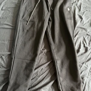 Svarta mjukisbyxor från Polo Ralph Lauren - Svarta mjukisbyxor från Polo Ralph Lauren med dragsko i midjan och broderad vit logga på benet. Byxorna har normal passform och är tillverkade i mjukt bomullsmaterial. Perfekta för en avslappnad stil.