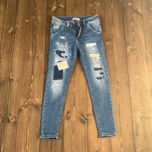 Blå slitna jeans med patchwork från Love Forever - Säljer ett par blå jeans med skinny passform från Love Forever. Jeansen har flera slitningar och patchwork-detaljer i olika tyger, bland annat paisleymönstrad och mörk denim. Klassisk femficksmodell med knapp och dragkedja.