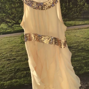 Champagnefärgad klänning med paljettdetaljer från Lindex - Gräddvit sidenklänning guldiga paljetter vid halsringen och vid midjan, storlek 158 och köpt på Lindex. Klänningen har en volangig kjol och är ärmlös, perfekt för speciella tillfällen💕🫶🏼🫧