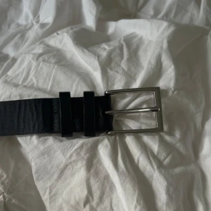 Svart bälte  - Stilrent svart bälte i skinn med ett klassiskt silverfärgat, fyrkantigt spänne. Bältet har en slät yta och flera hål för justering. Bältet är köpt ifrån Lindex, har inte prislappen kvar men är aldrig använt!🤍🤍