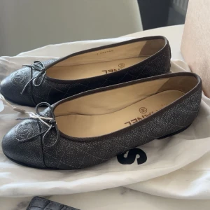 Svarta ballerinaskor från Chanel -  klassiska svarta ballerinaskor från Chanel i skinn med quiltat mönster och rosett framtill. Skorna har rund tå strl 36,5