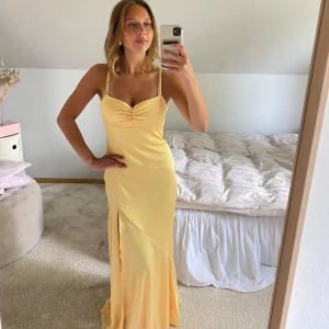 Ljusgul långklänning med slits - Säljer en elegant ljusgul långklänning med smala axelband och v-ringad byst. Klänningen har en hög slits framtill och är sydd i ett glansigt, satinliknande material som ger en lyxig känsla. Perfekt för sommarens speciella tillfällen som bal och student gäst och sommarfester, sittningar osv!!