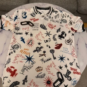 Vit t-shirt med grafiska tryck och svart krage - Vit t-shirt från Zar* med svart krage och massor av grafiska tryck i rött, svart och blått. Trycken består av olika symboler, texter och illustrationer som ger en unik och edgy look. Perfekt för dig som vill sticka ut.