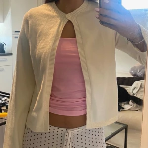 Vit stickad bolerotopp - Säljer en krämvit stickad bolerotopp med rund halsringning och knapp framtill. Toppens material är mjukt och har ribbade kanter. Perfekt att slänga över ett linne eller klänning för en extra touch. Använd 1 gång!