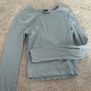 Ljusblå långärmad topp från Gina Tricot - Säljer en ljusblå långärmad topp från Gina Tricot i ribbat material. Toppen har en croppad passform med vågig kant nertill och en stor öppen rygg. Perfekt för dig som gillar stilrena men ändå unika detaljer. Står storlek XS, passar även S