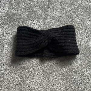 Svart ribbat pannband från McKinley - Chunky svart pannband från McKinley med twistad design framtill. Ribbad struktur som ger en cool och enkel look. Tillverkat av mjuk akryl, nylon och elastan för skön passform. Perfekt för att hålla öronen varma under kyliga dagar.