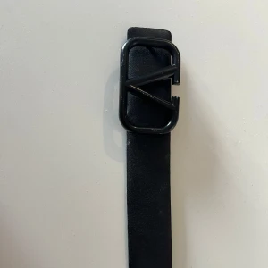 Valentina skärp - Snyggt svart bälte med ett coolt, geometriskt metallspänne i svart. Bältet är stilrent och har en bred, rak form som passar till jeans eller byxor. Materialet är skinn och ger en klassisk vibe med en modern twist tack vare spännet.