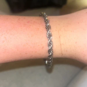 Flätat silver armband - Snyggt armband i silverfärg med flätad kedja som ger en cool och stilren look. Perfekt att bära ensam eller kombinera med andra smycken för en personlig stil. Lätt att ta på med smidig låsning.