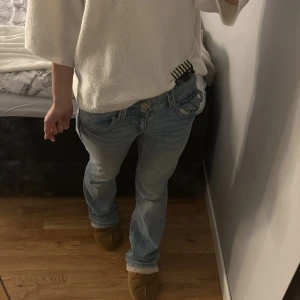 Ljusblå bootcut jeans låg midja - Säljer ett par ljusblå jeans med snygg bootcut passform och låg midja. Jeansen har klassisk femficksdesign, knapp och dragkedja framtill samt lätt slitna detaljer för en chill vibe. Perfekta för dig som gillar avslappnad stil och vill ha jeans som sitter skönt.