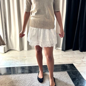 Vit volangkjol med broderade detaljer - Supersöt vit kortkjol med volanger och broderade blommor. Kjolen har elastisk midja och spetskant längst ner som ger en romantisk vibe. Perfekt att matcha med en stickad tröja. Lätt och luftig, passar grymt till varma dagar. Den är oanvänd! Stolek xs/S. 