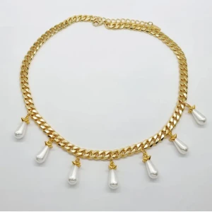 Guldfärgat halsband med pärldroppar - Chunky guldfärgat halsband med sju hängande droppformade pärlor i vitt. Kedjan är bred och glänsande, och pärlorna har små guldfärgade detaljer upptill. Perfekt statement-piece för dig som vill sticka ut med en elegant och trendig look.