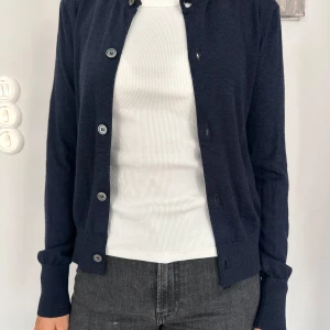 Mörkblå kofta från Acne Studios - Snygg mörkblå kofta från Acne Studios med rund hals och knappar framtill. Mjuk och tunn stickad kvalitet, perfekt att slänga över en t-shirt. Långärmad och med ribbade muddar vid ärmslut och nederkant. Enkel och stilren design som funkar till allt.