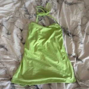 Limegrön topp med öppen rygg med snörning - Snygg limegrön topp med halterneck och snörning i ryggen. Klänningen har omlott-detaljer på sidorna och är tillverkad i mjuk bomull. Perfekt för dig som gillar färgstarka och trendiga plagg med en cool vibe.