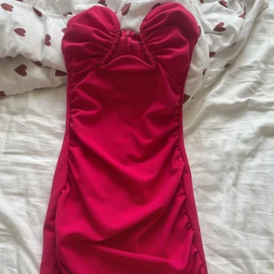 Rosa kort klänning från Gina Tricot - Säljer en snygg och figurnära kort klänning från Gina Tricot i en stark rosa färg. Klänningen har en låg urringning med rynkade detaljer upptill och dragkedja i sidan. Perfekt för dig som vill sticka ut med en cool och trendig look. Köptes för 399kr och aldrig använd💞