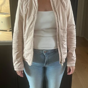 Ljusrosa bomberjacka från Jofama - Snygg ljusrosa bomberjacka från Jofama med quiltade detaljer på ärmarna. Jackan har dragkedja framtill och ett blommigt mönster på insidan. Perfekt för dig som vill ha en stilren och trendig look.