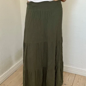 Grön sommarkjol - Säljer en fin somrig olivgrön maxikjol från lager 157 i storlek S. Materialet är mjukt och lätt och kjolen är sydd i flera flowiga lager. 