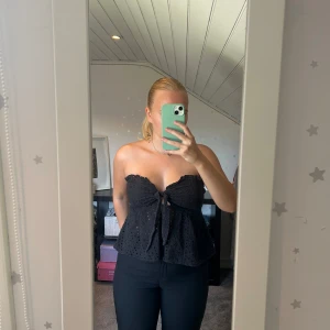 Svart bandeau tubtopp med knyt - Säljer en svart bandeau tubtopp med broderade hålmönster och volangkant, toppen har även ett sött knyt framtill. Djur finns i hemmet! 🩷