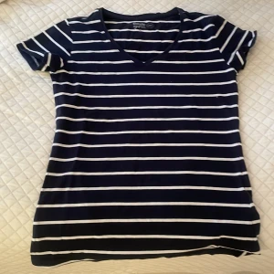 Randig navy t-shirt från Basic You - navyblå och vit randig t-shirt från Basic You i ekologisk bomull. Modellen har v-ringad hals och korta ärmar. Skön passform som sitter normalt och känns mjuk mot huden. Enkelt och stilrent plagg som funkar till jeans eller shorts.