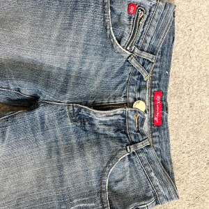 Lågmidjade raka jeans från Jox - Snygga blå jeans från Jox med slitna detaljer och raka ben. Klassisk femficksmodell med dragkedja och knapp framtill. Jeansen har ljus tvätt och coola slitningar på både fram- och bakbenen. Endast använda en gång